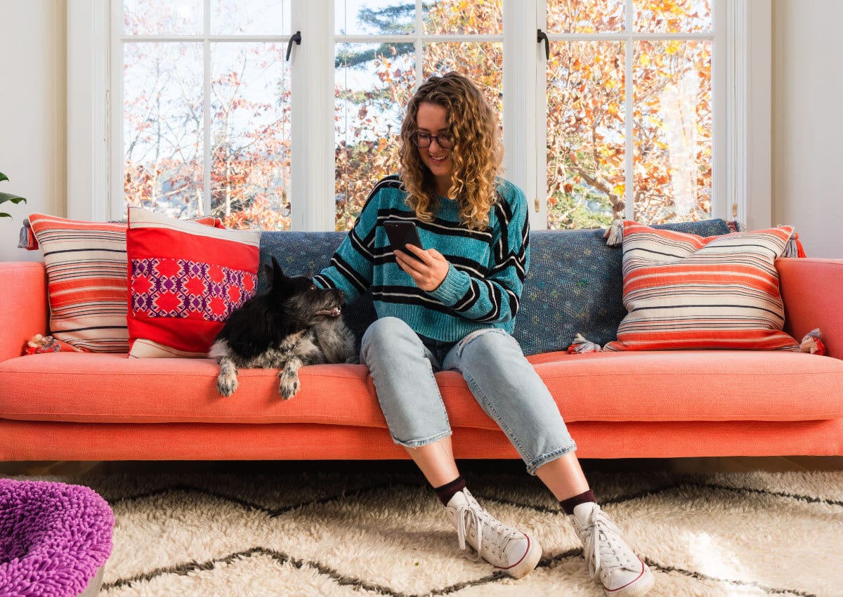 Woman sits on couch looking at phone while petting dog