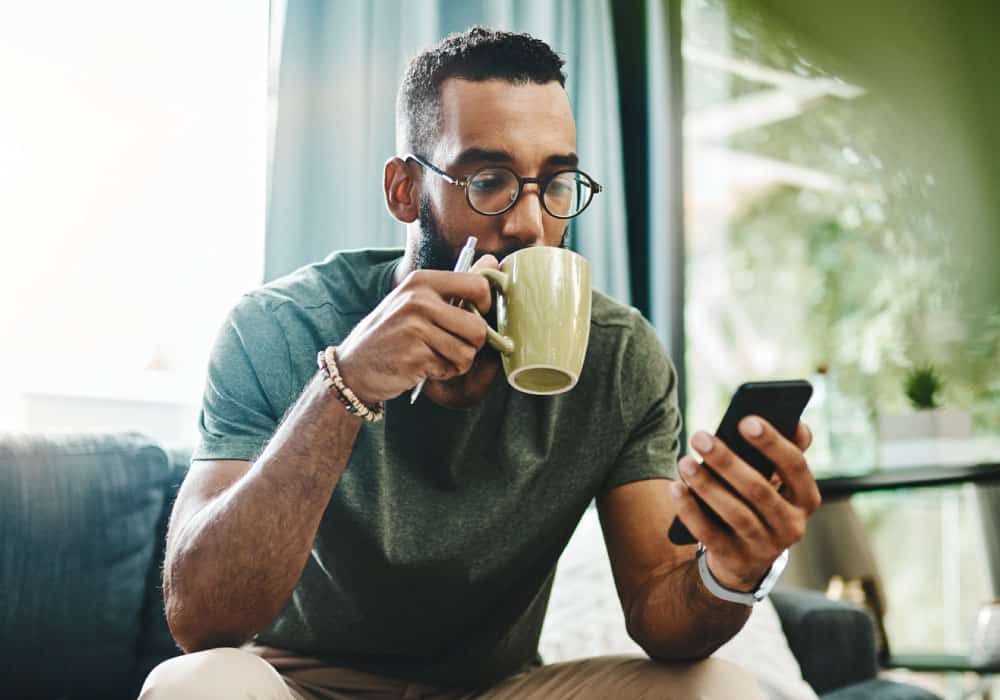 man sips coffee while checking phone