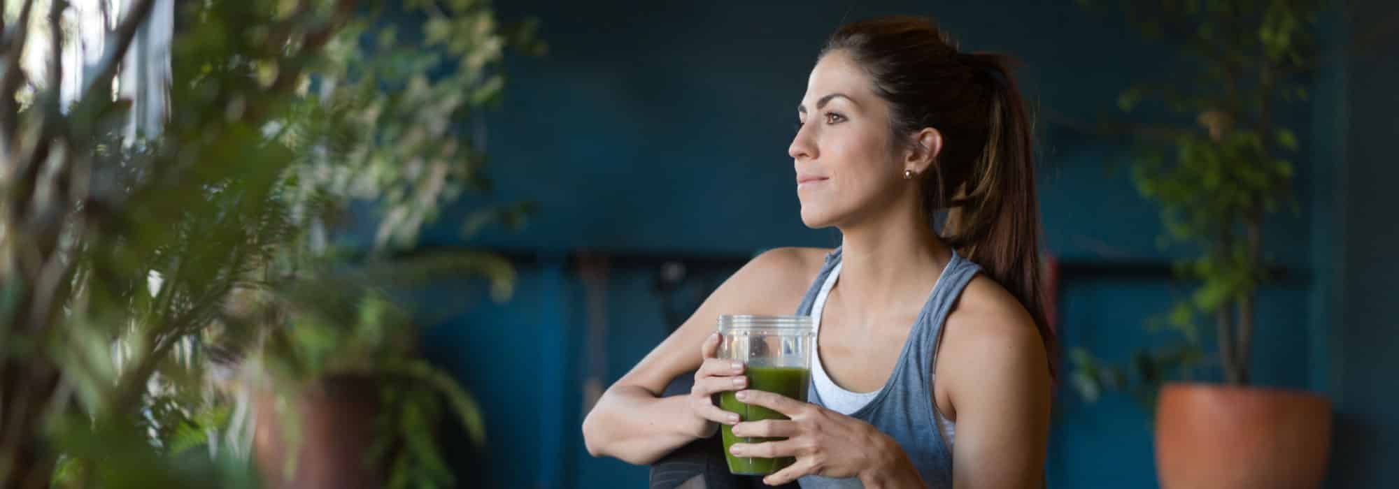 A woman sitting down and drinking a green smoothie.