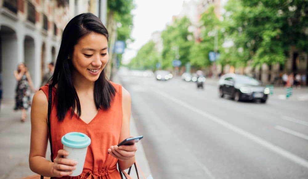 A woman walking around outside, she is looking down at a phone and smiling.