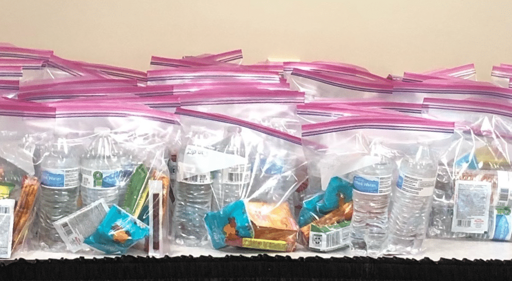 Plastic zip bags are arranged on a table and hold items like water bottles and snacks