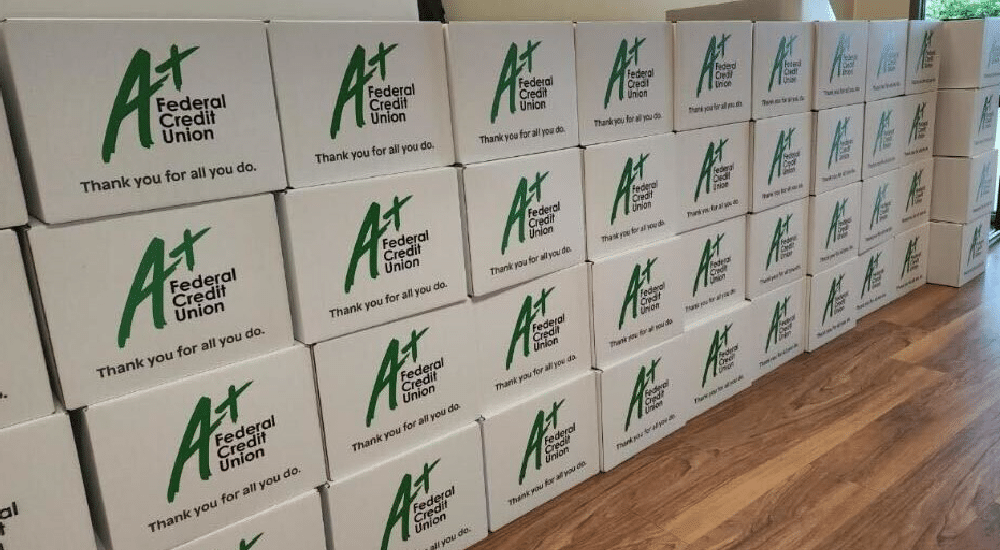 White boxes with the A+FCU logo and “Thank you for all you do.” are stacked on the floor