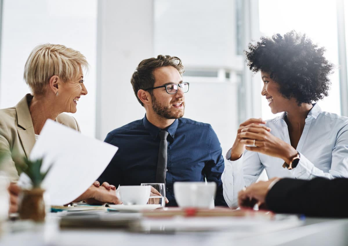 Three people sitting at a table in an office and looking over paperwork.