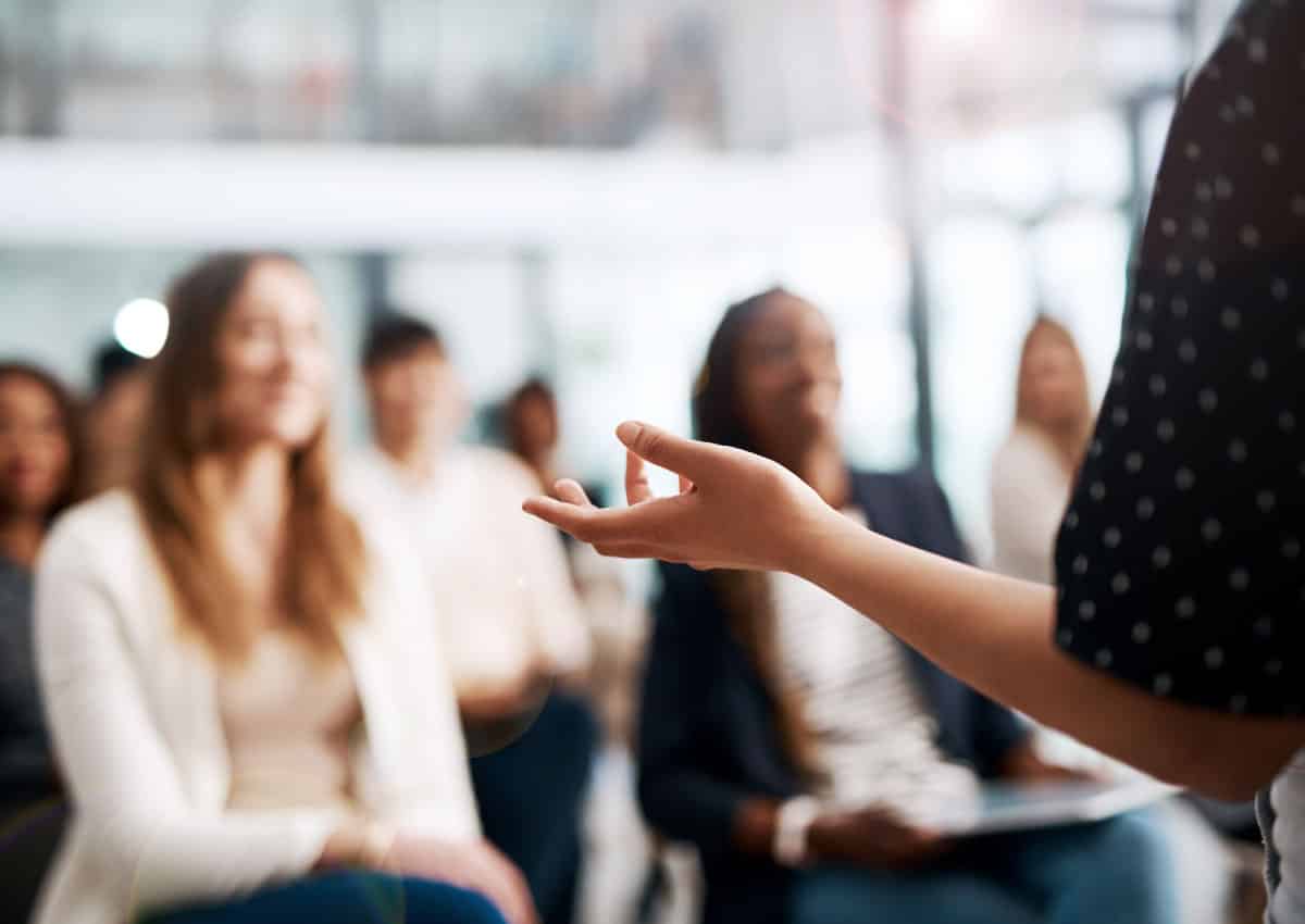 A woman is standing in front of a room and giving a presentation.