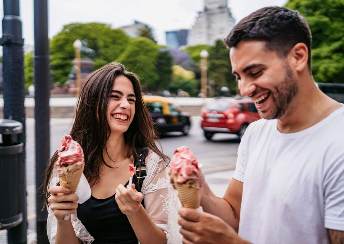 A man and a woman eating ice cream and walking, they are smiling.