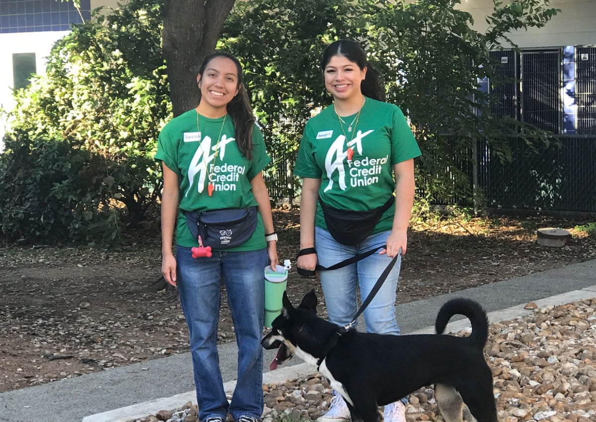 Two A+FCU volunteers stand outside the Austin Animal Center with a dog on a leash.