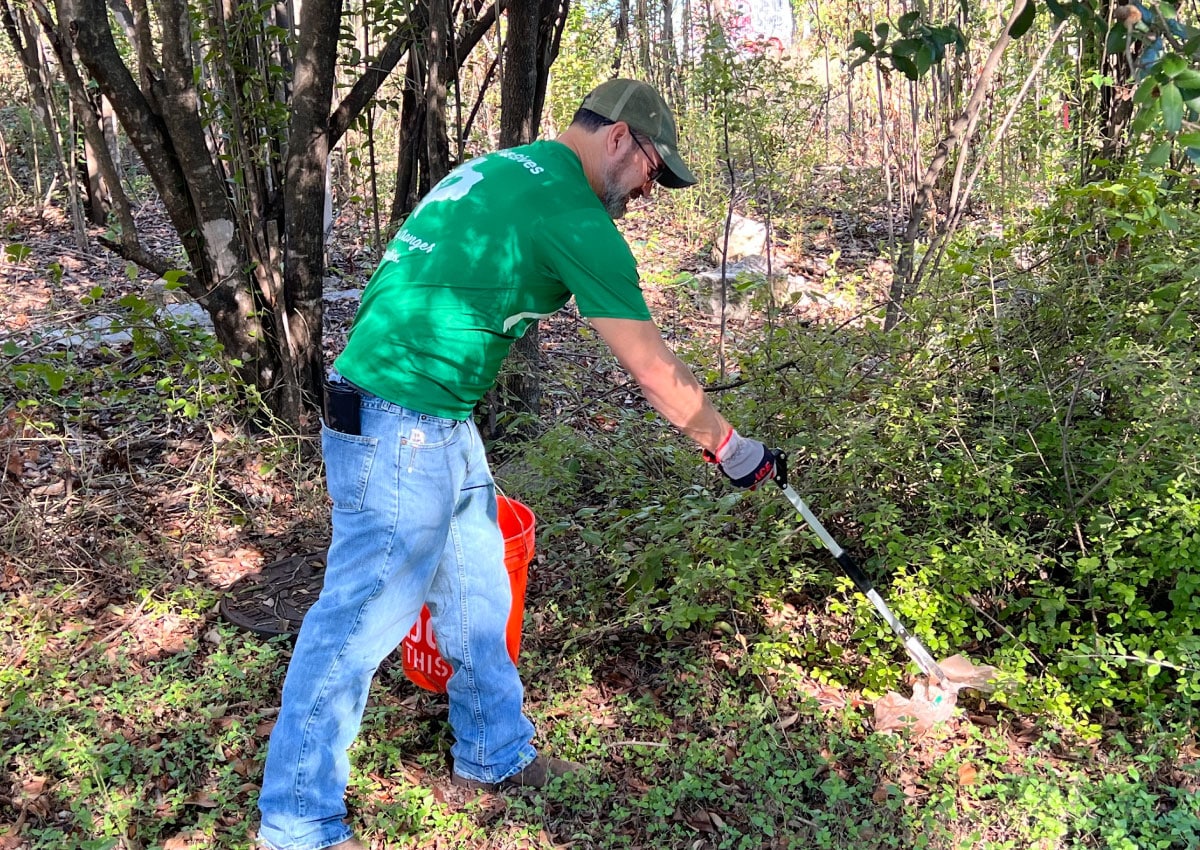 An A+FCU volunteers pick up trash on a path at a park in Austin.