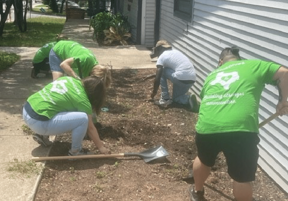 Group of A+ volunteers work in a dirt bed with shovels