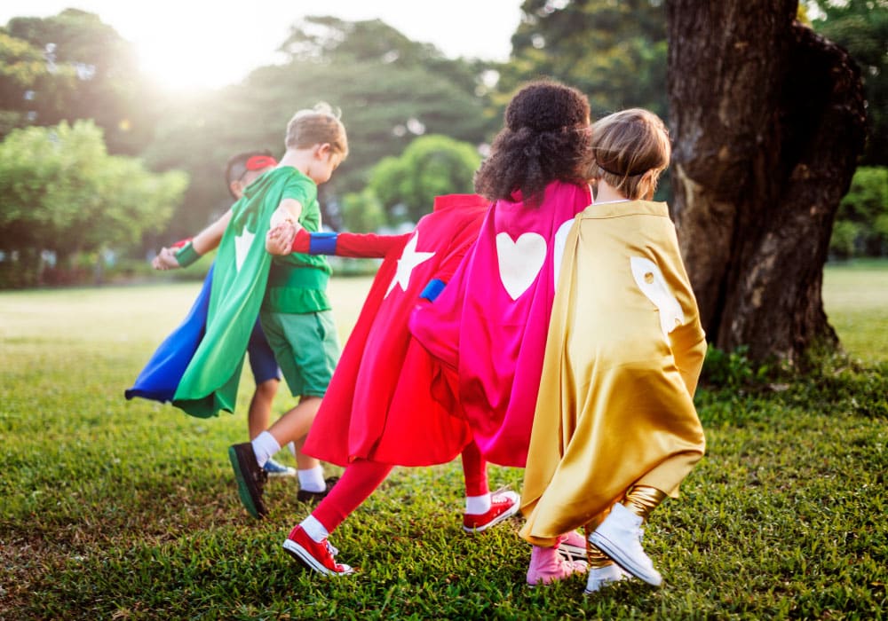 Kids wearing capes and superhero attire run around outside