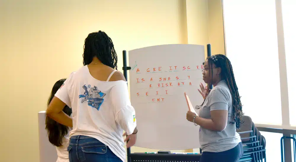 People gathered around a whiteboard, discussing notes in a bright classroom setting.