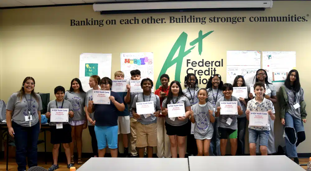 Diverse group of kids and teens posing with certificates at a credit union youth camp ceremony.
