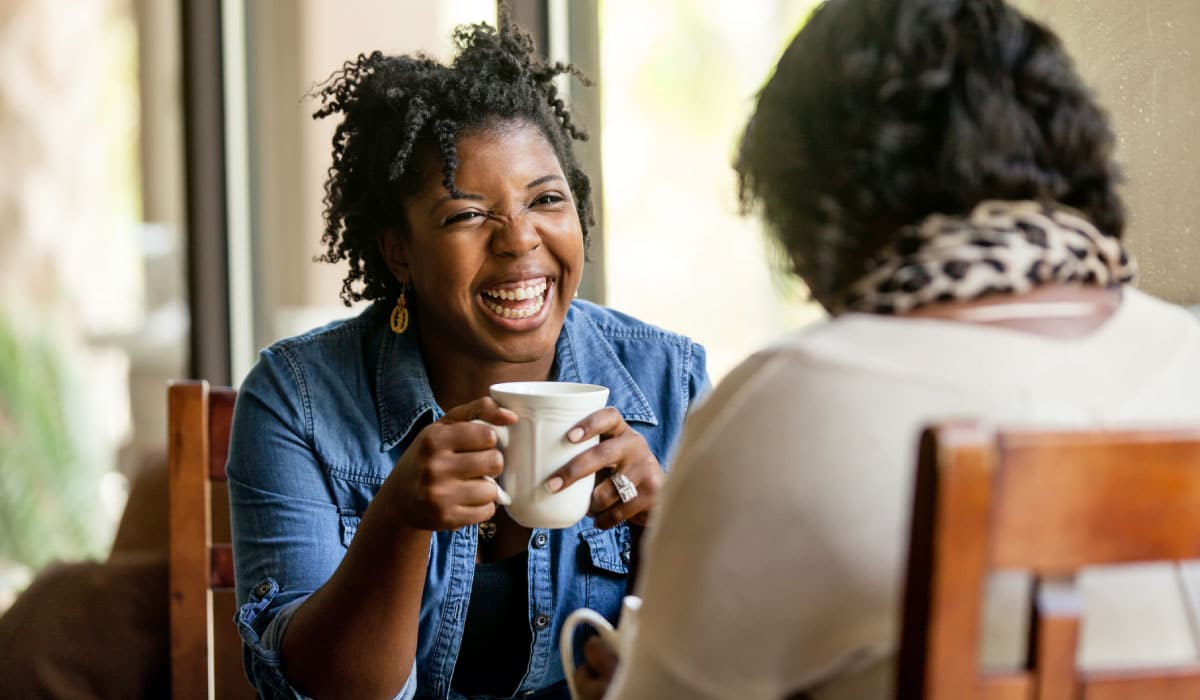 two women sharing coffee and laughing.