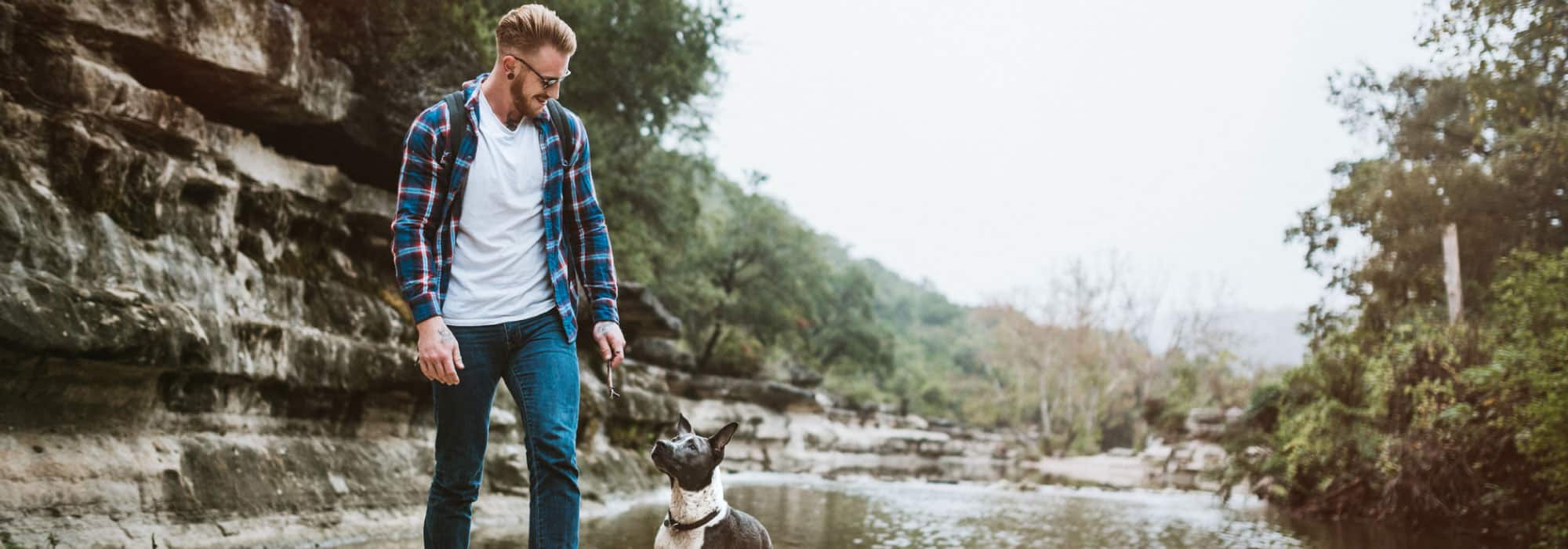 A man walks through a creek with a dog.