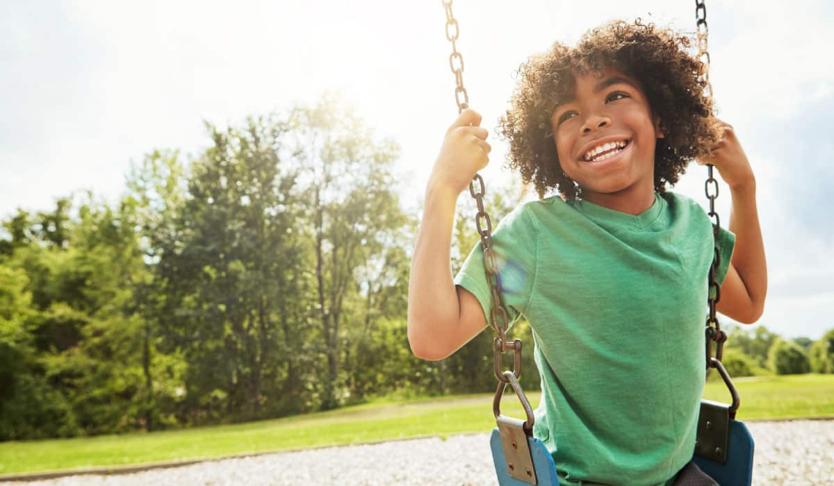 A boy sits on a swing, he is smiling and laughing.