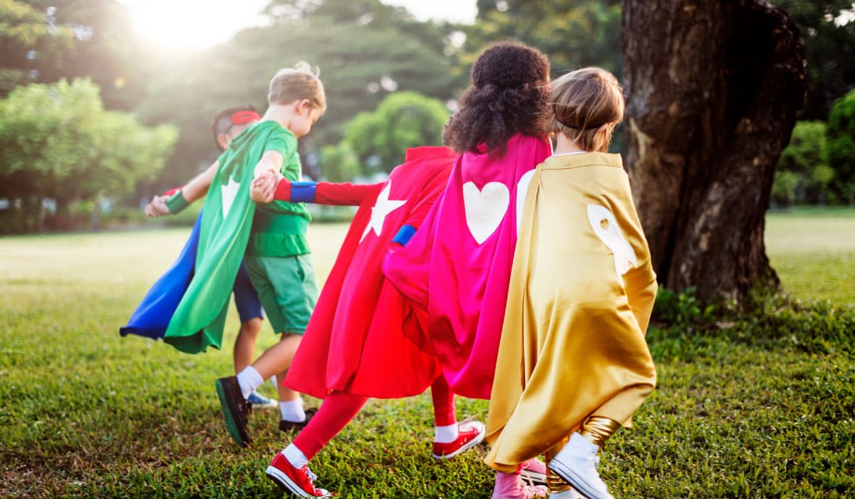 A group of children wearing halloween costumes and running through a field.
